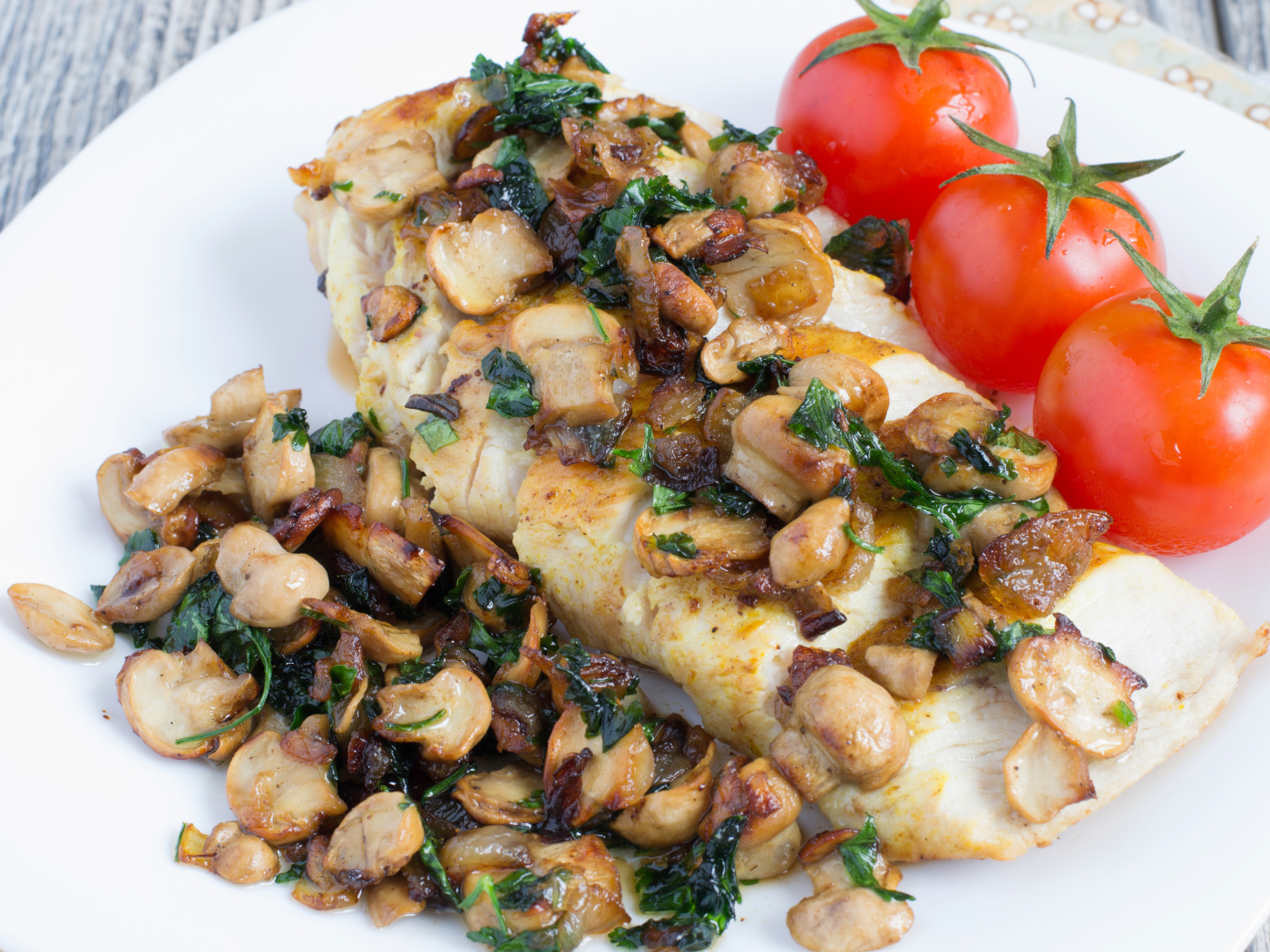 Аппетитный кусок куриного филе с грибами на тарелке с помидорами 