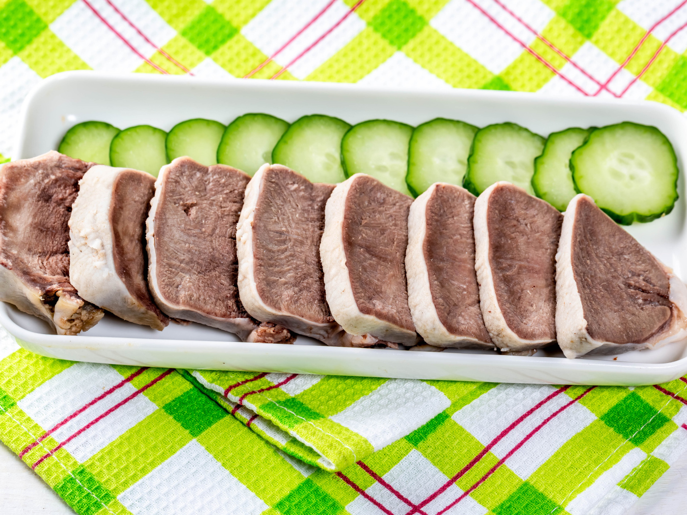 Вареный язык на тарелке со свежими огурцами