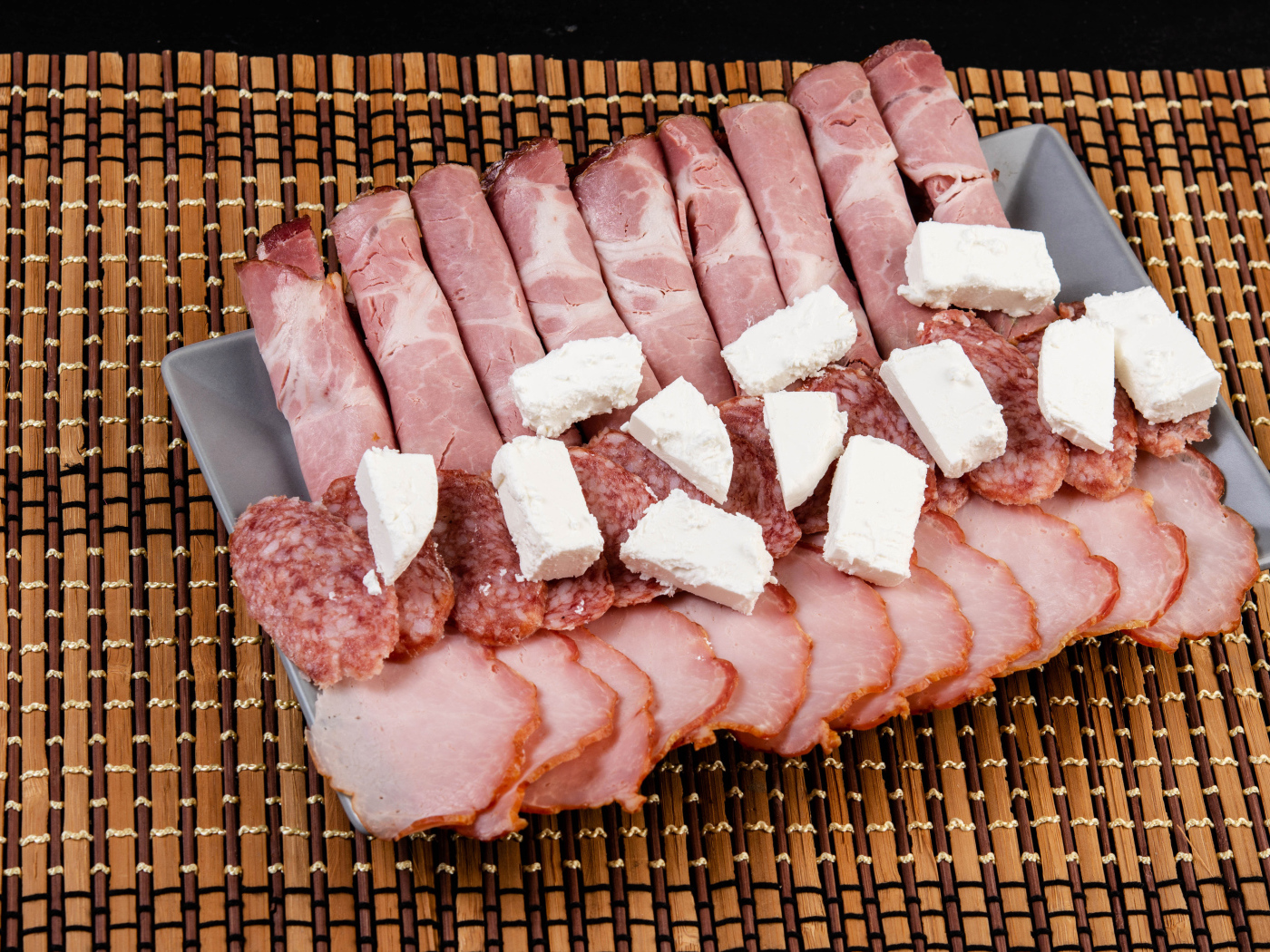 Колбаса и ветчина на тарелке с кусочками сыра фета