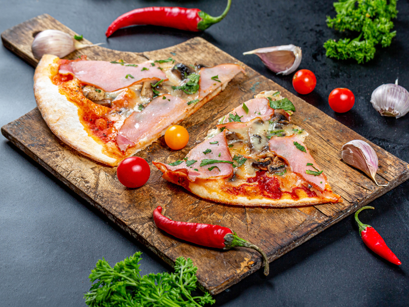 Два куска пиццы на разделочной доске с красным перцем и чесноком