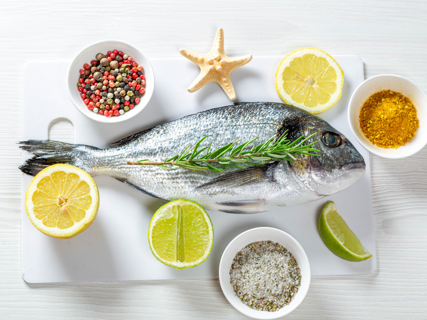 Свежая рыба на доске с солью, перцем, куркумой и лимоном