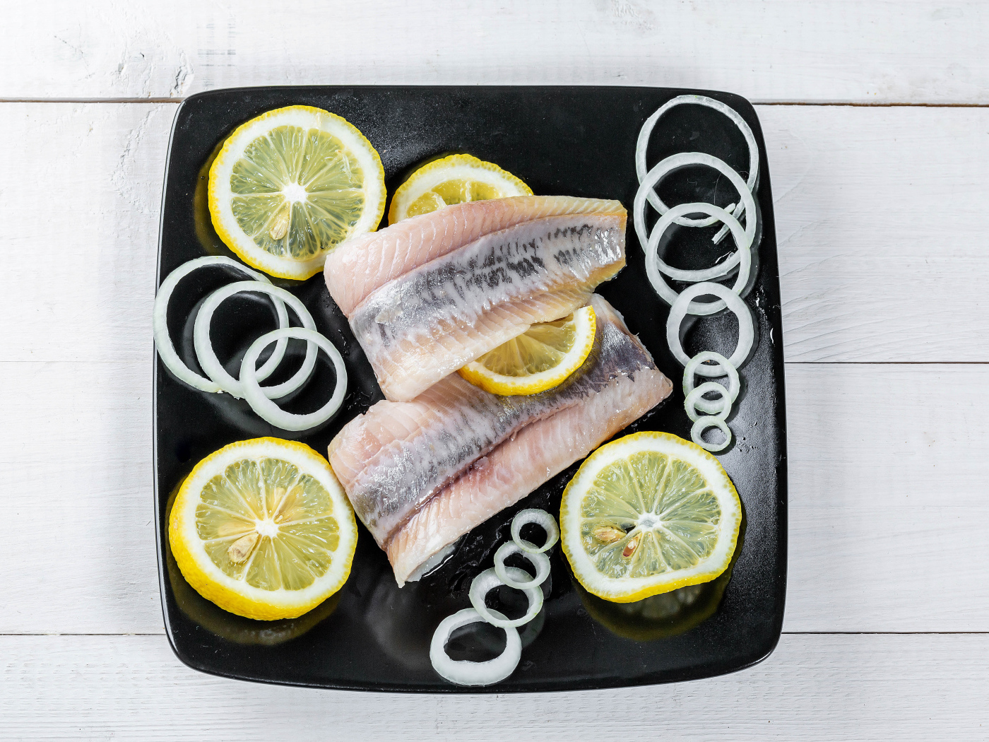 Филе сельди на черной тарелке с луком и лимоном