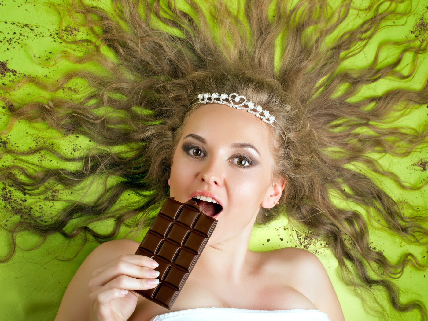Красивая девушка с украшением в волосах лежит с шоколадкой 