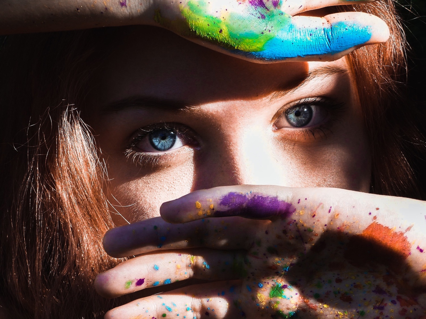 Красивая голубоглазая девушка с руками в разноцветной краске у лица
