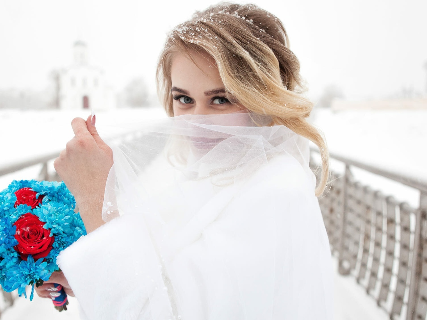 Красивая невеста с букетом в руках закрывает лицо фатой