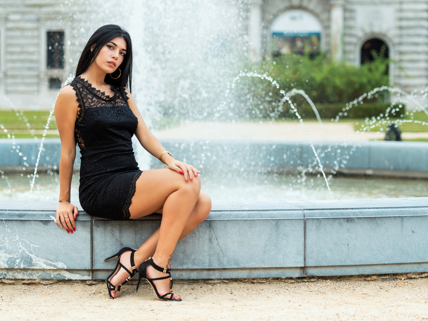 Красивая брюнетка в черном платье сидит у фонтана