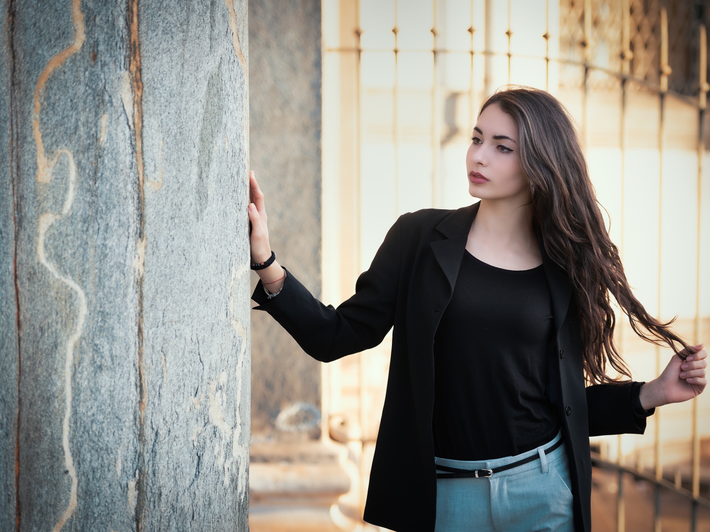 Красивая девушка в черном пиджаке стоит у стены