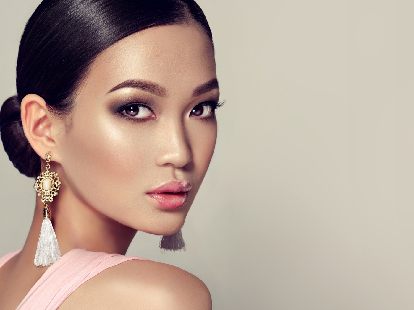 Красивая девушка с прической и сережками в ушах на сером фоне