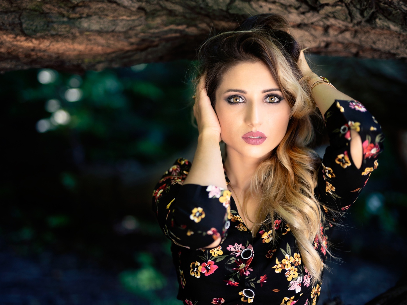 Красивая девушка с руками в волосах у дерева