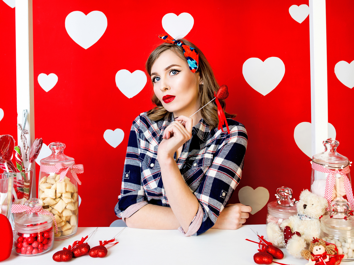 Яркая девушка за столом со сладостями на красном фоне с белыми сердечками 