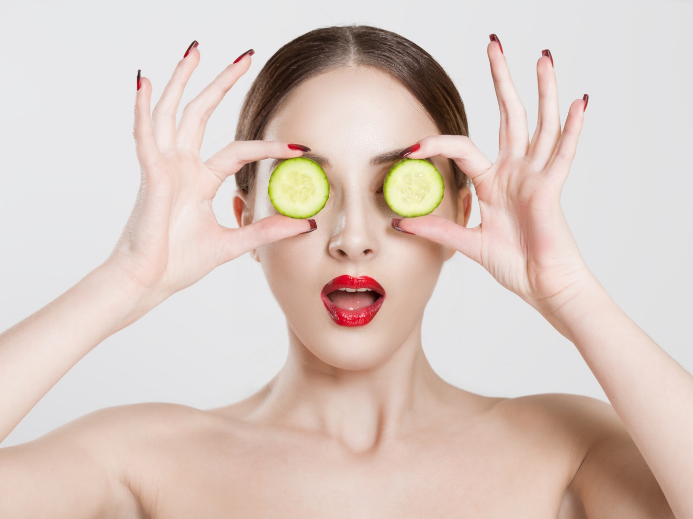 Яркая девушка с огурцами у глаз на сером фоне