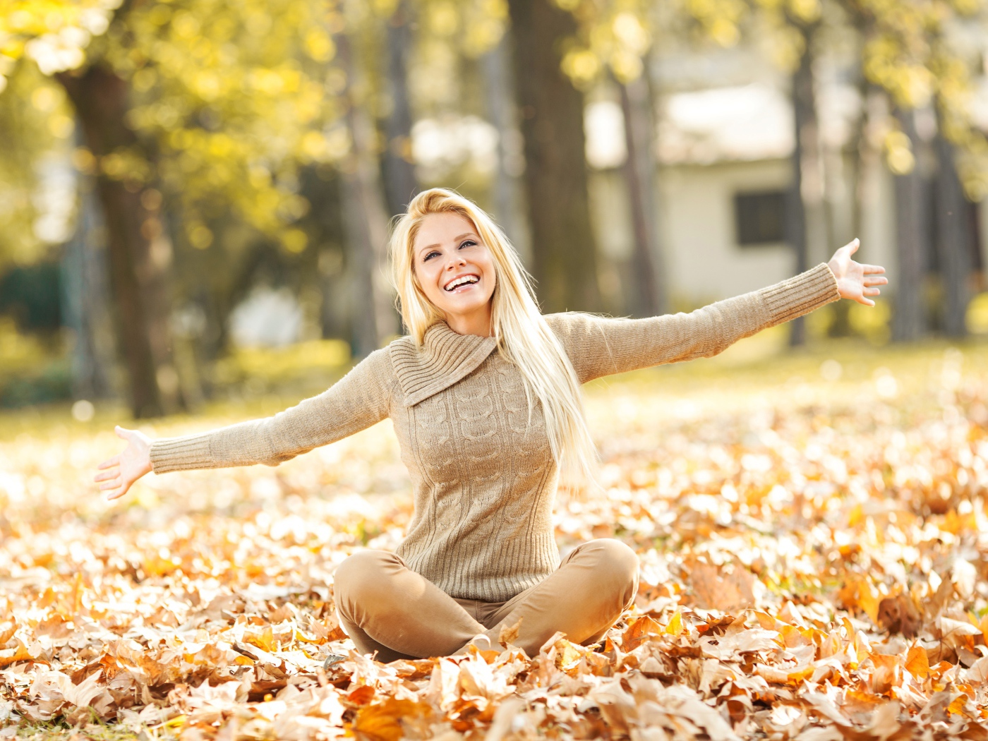 Веселая девушка сидит на опавшей листве осенью 