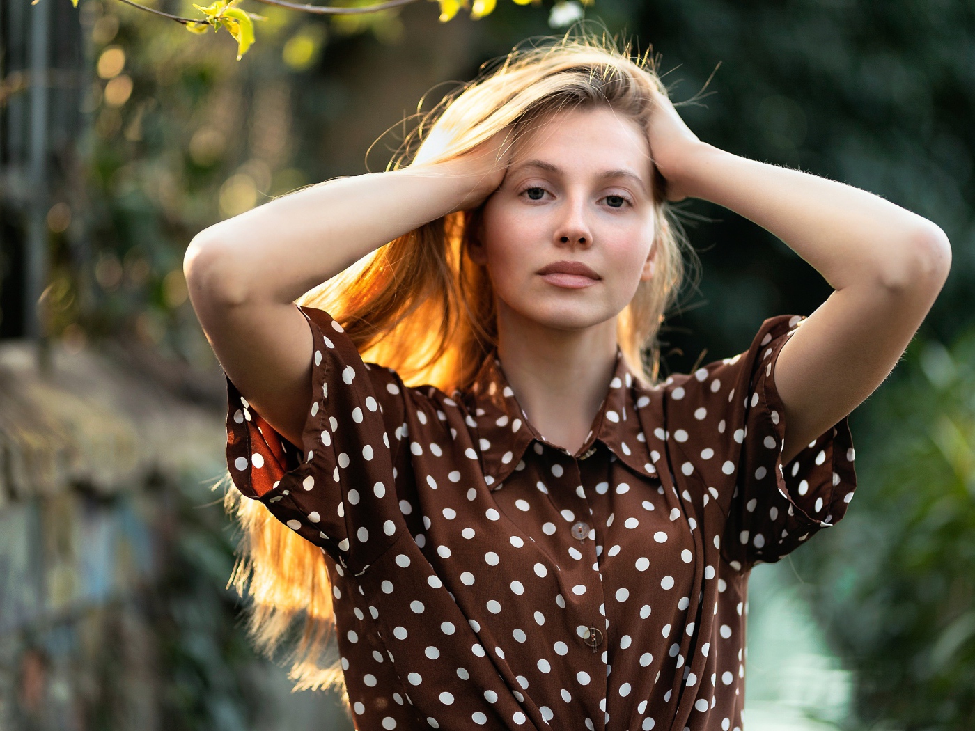 Девушка в рубашке в горох с руками в волосах 