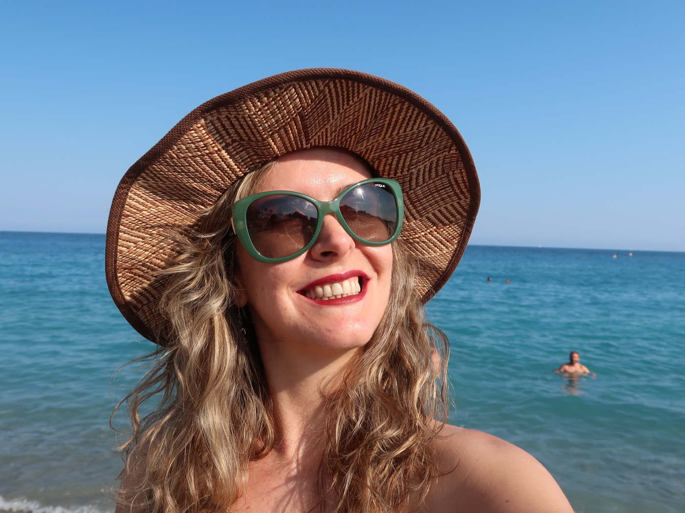 Улыбающаяся девушка в солнечных очках и шляпе на море