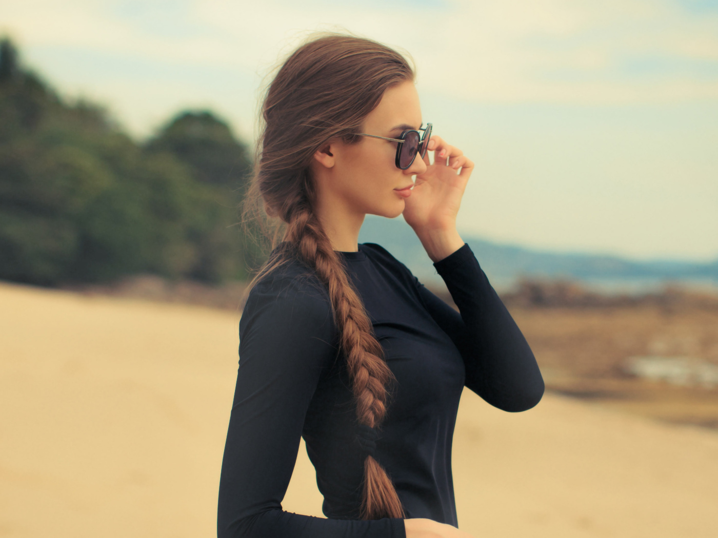 Девушка с косой в черных очках смотрит на воду