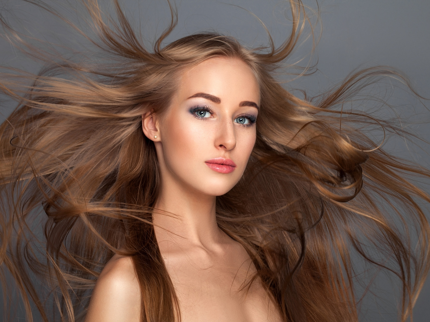 Ветер развивает волосы красивой девушке на сером фоне
