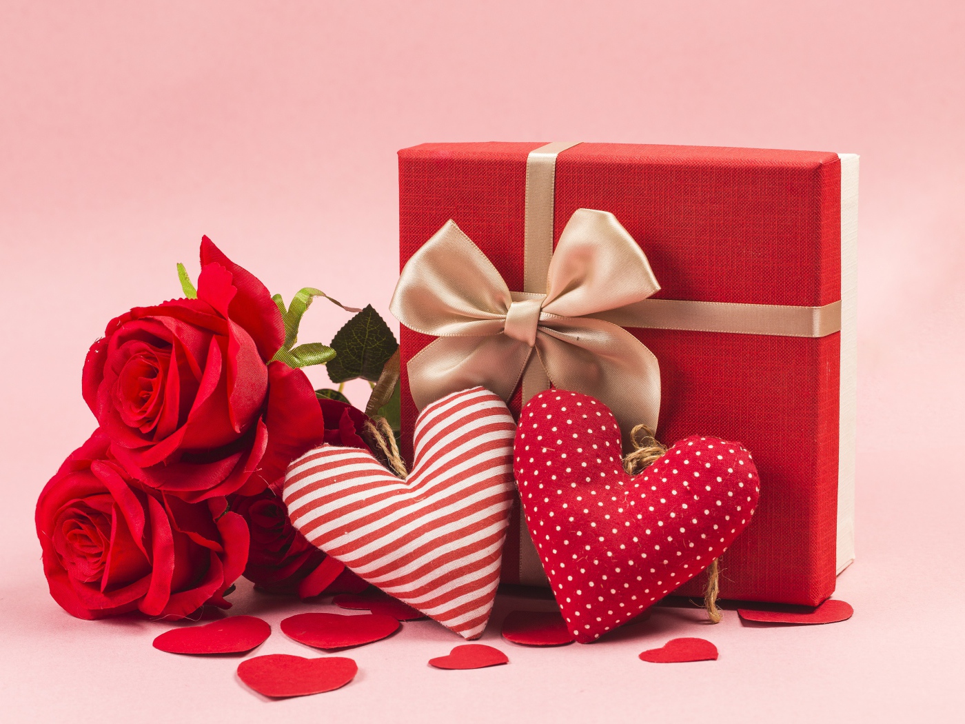 Three red roses with hearts and gift on a pink background