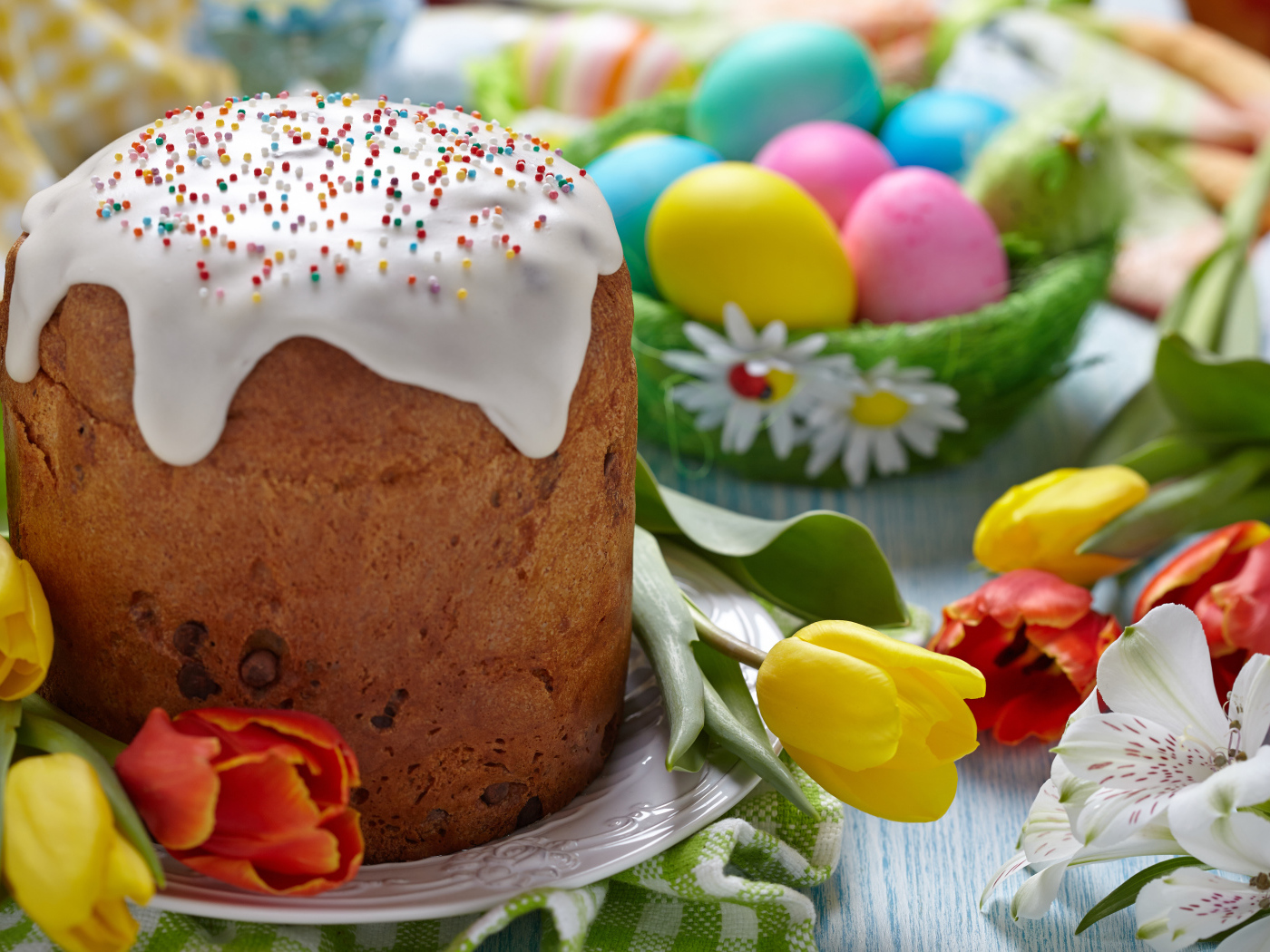 Пасхальный кулич на столе с тюльпанами и крашеными яйцами