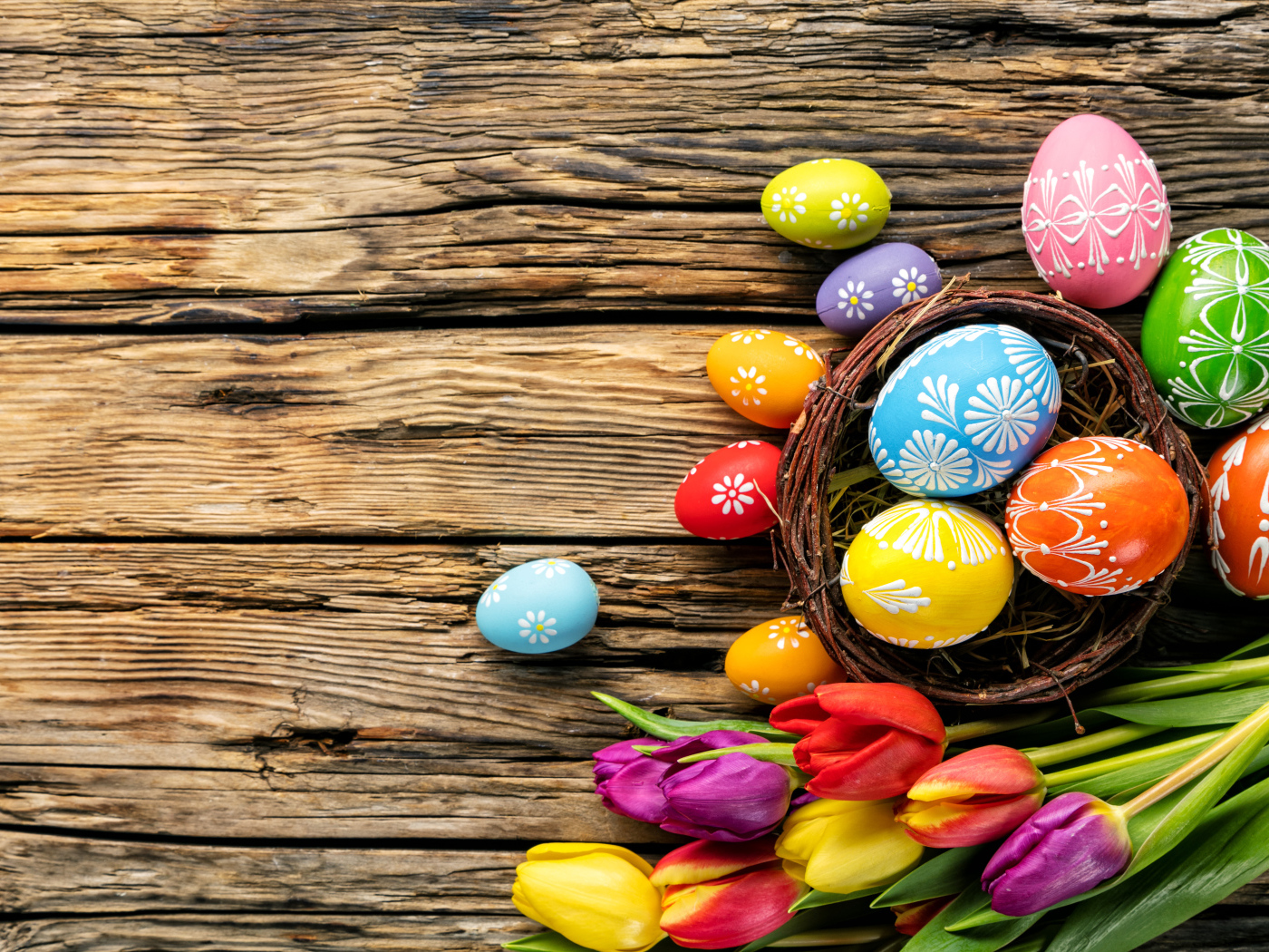 Крашеные пасхальные яйца с букетом тюльпанов на деревянном фоне