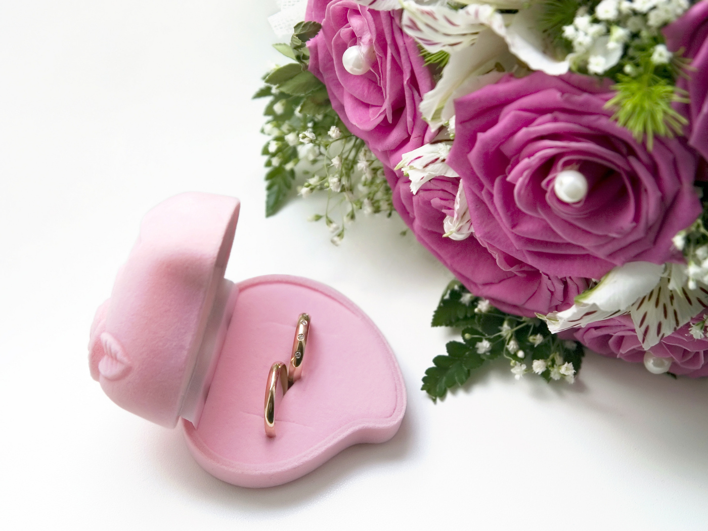 Два обручальных кольца в коробочке на белом фоне с букетом роз