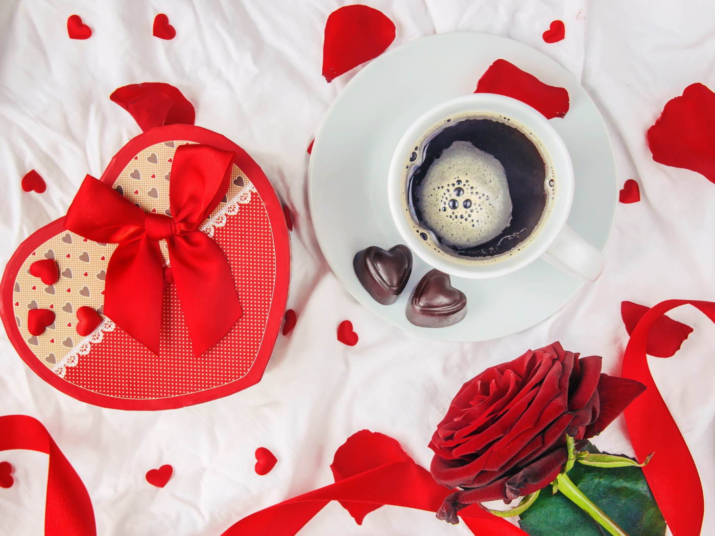 Кружка с кофе и шоколадными конфетами на столе с подарком и красной розой 