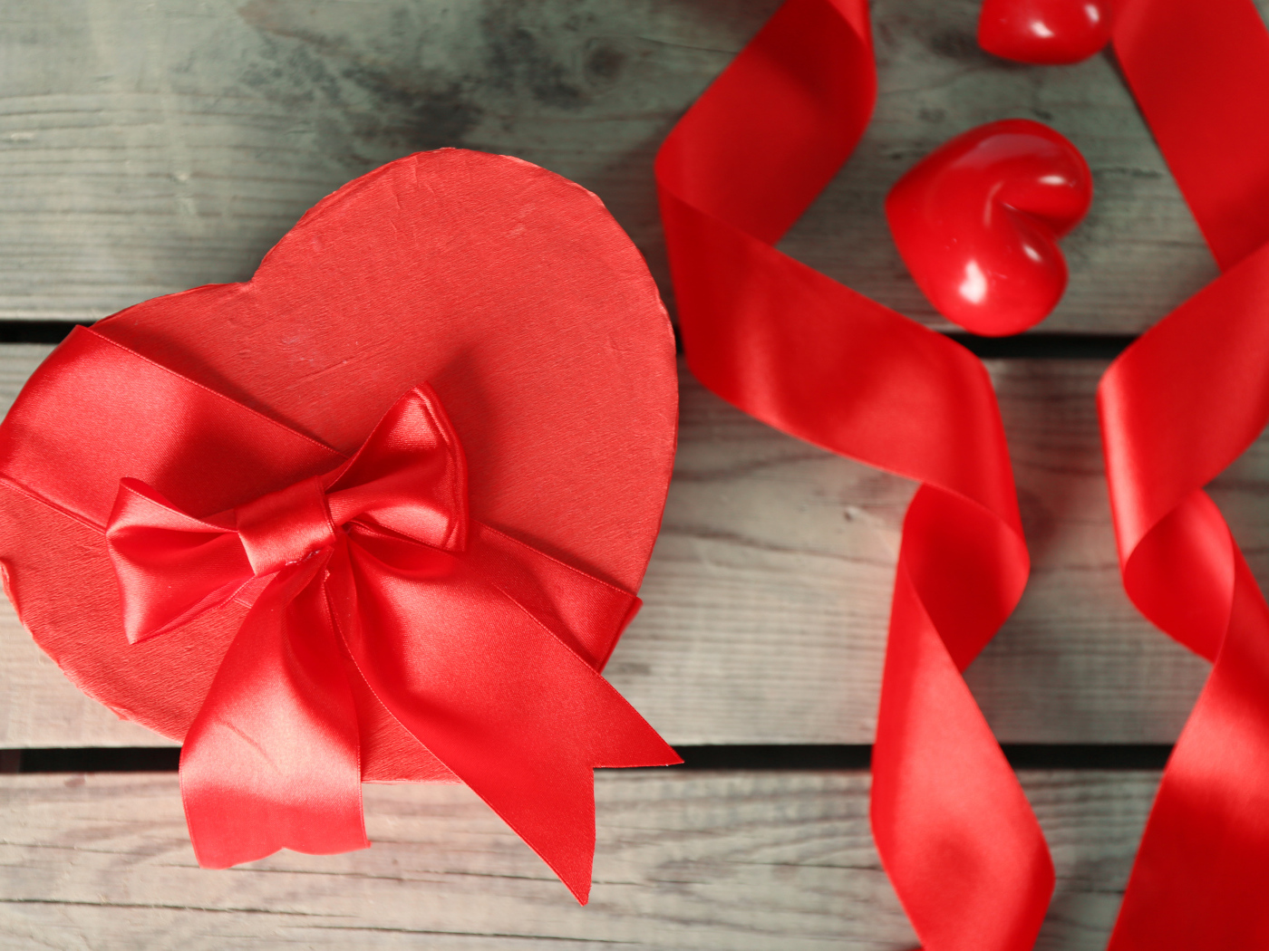 Красная коробка в форме сердца на деревянном столе с красными лентами