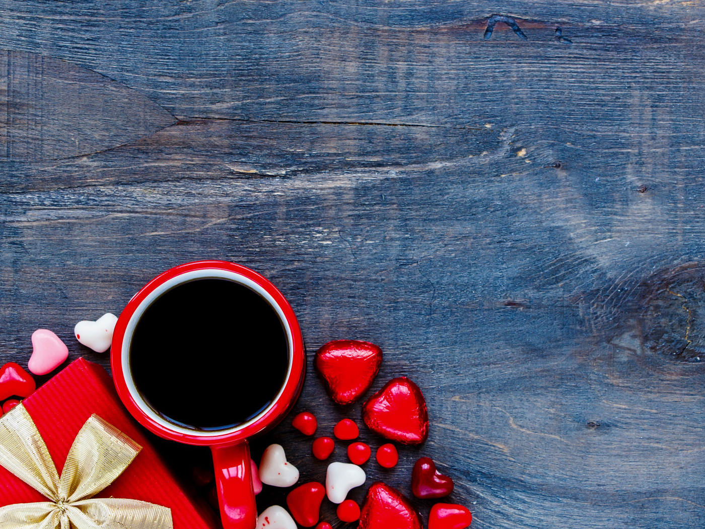 Красная чашка кофе, сердечки и подарок на деревянном фоне