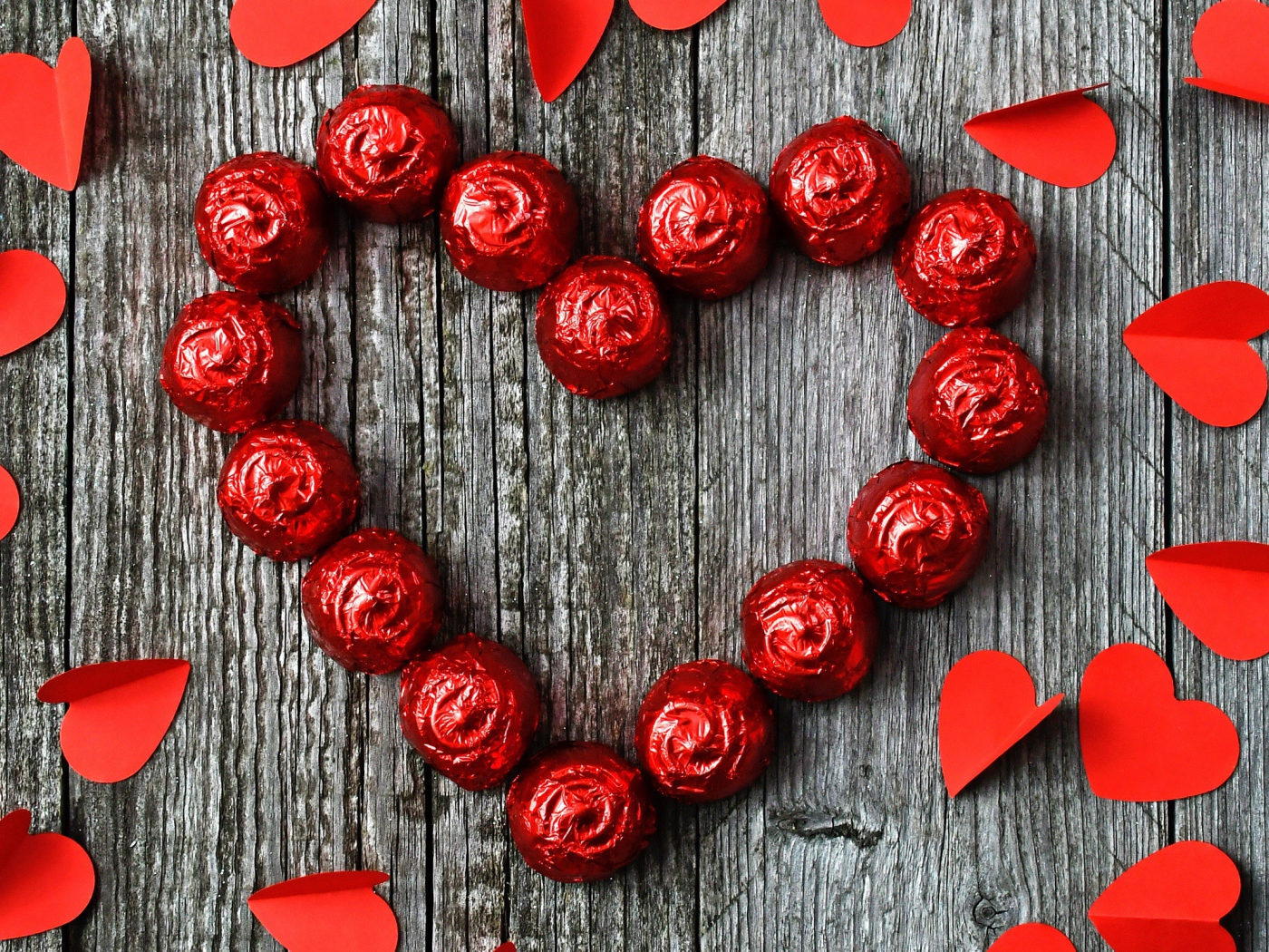 Красное сердце из конфет на деревянном фоне с бумажными сердечками