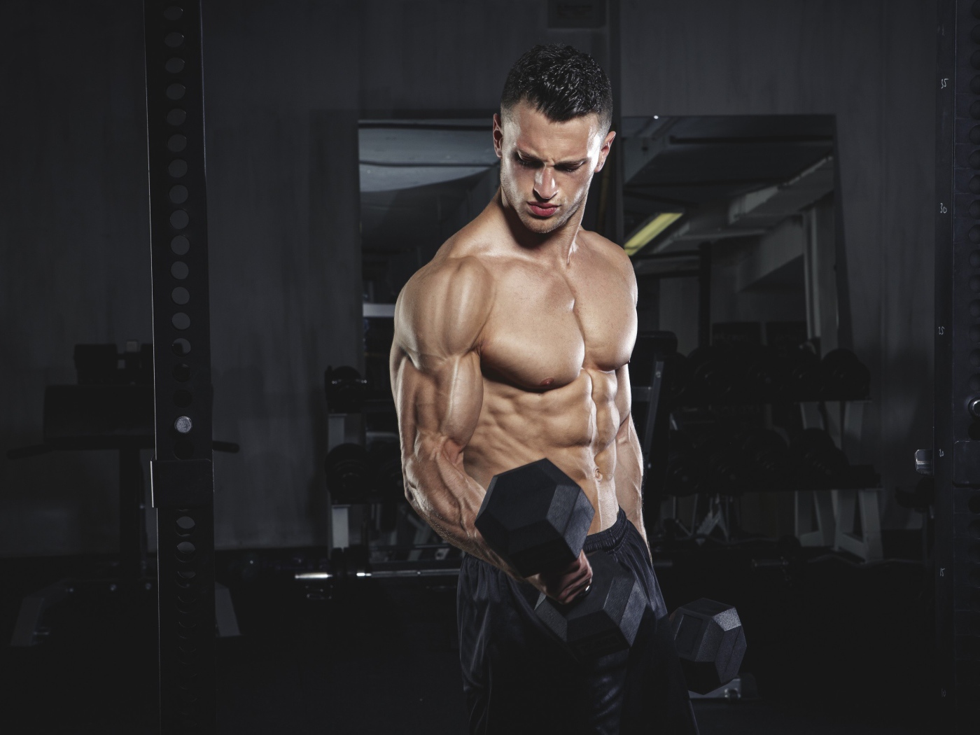 Накаченный мужчина с тяжелыми гантелями в руках 