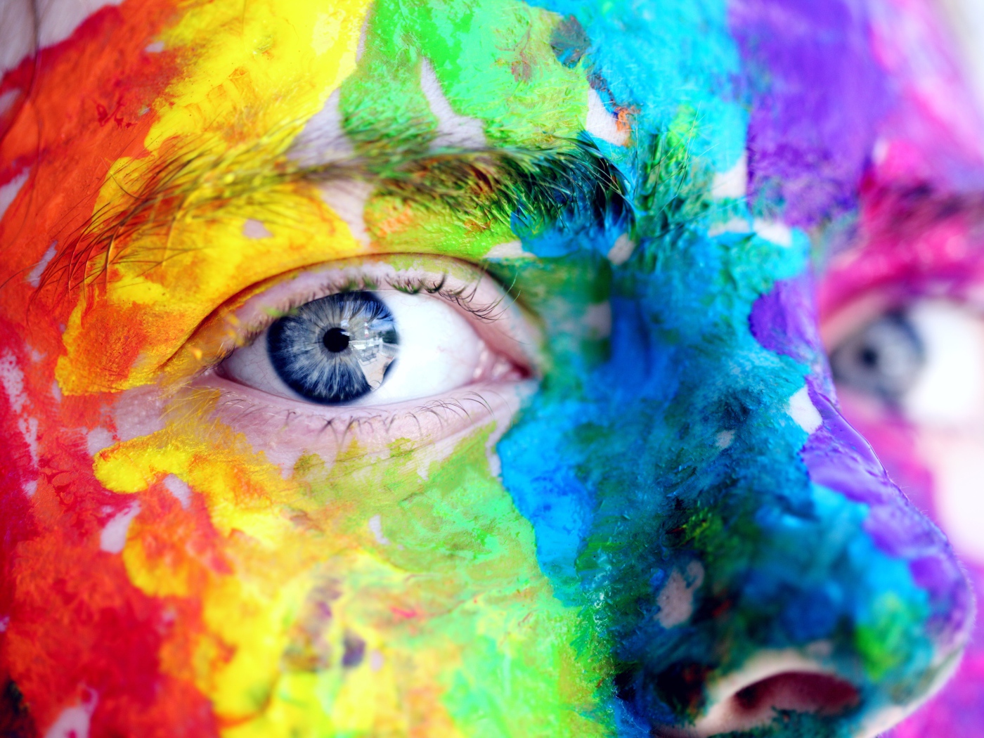 The face of a blue-eyed man in multi-colored paints close-up