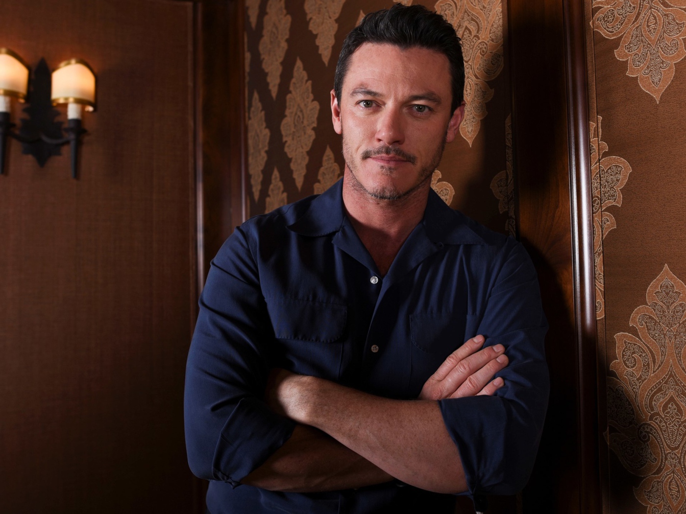 Актер Люк Эванс в рубашке стоит у стены