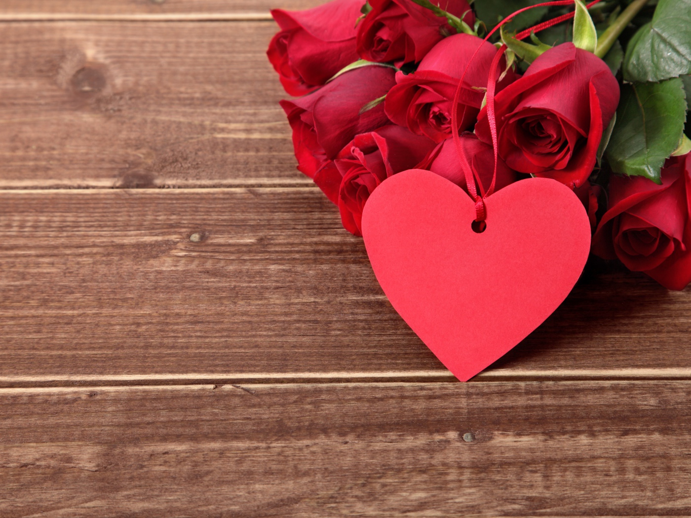 Букет красных роз на деревянном столе с красным сердцем