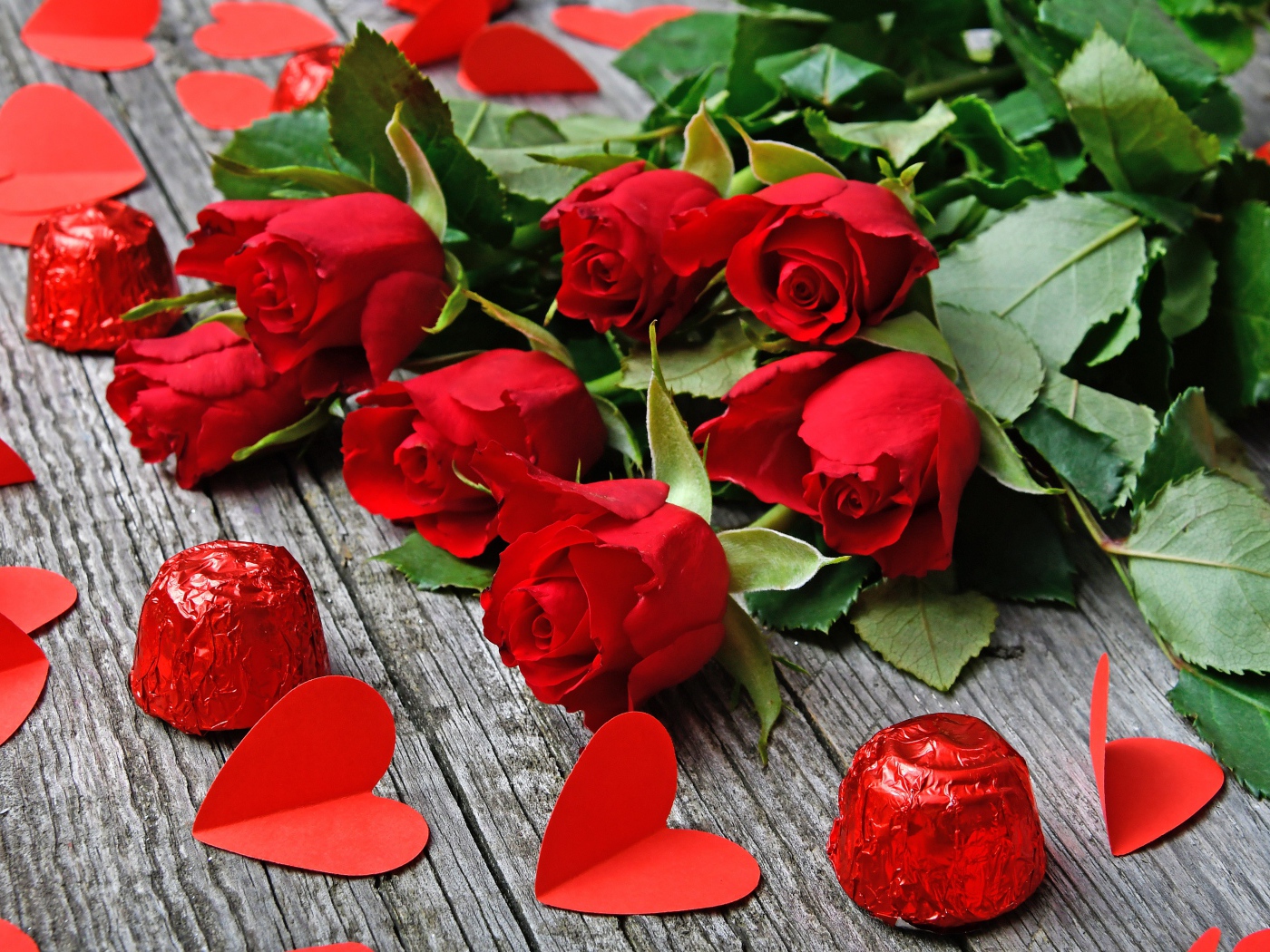 Букет красных роз на деревянном столе с конфетами и красными сердечками
