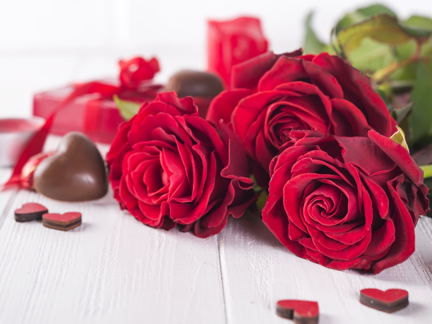 Три красивые красные розы на столе с конфетами