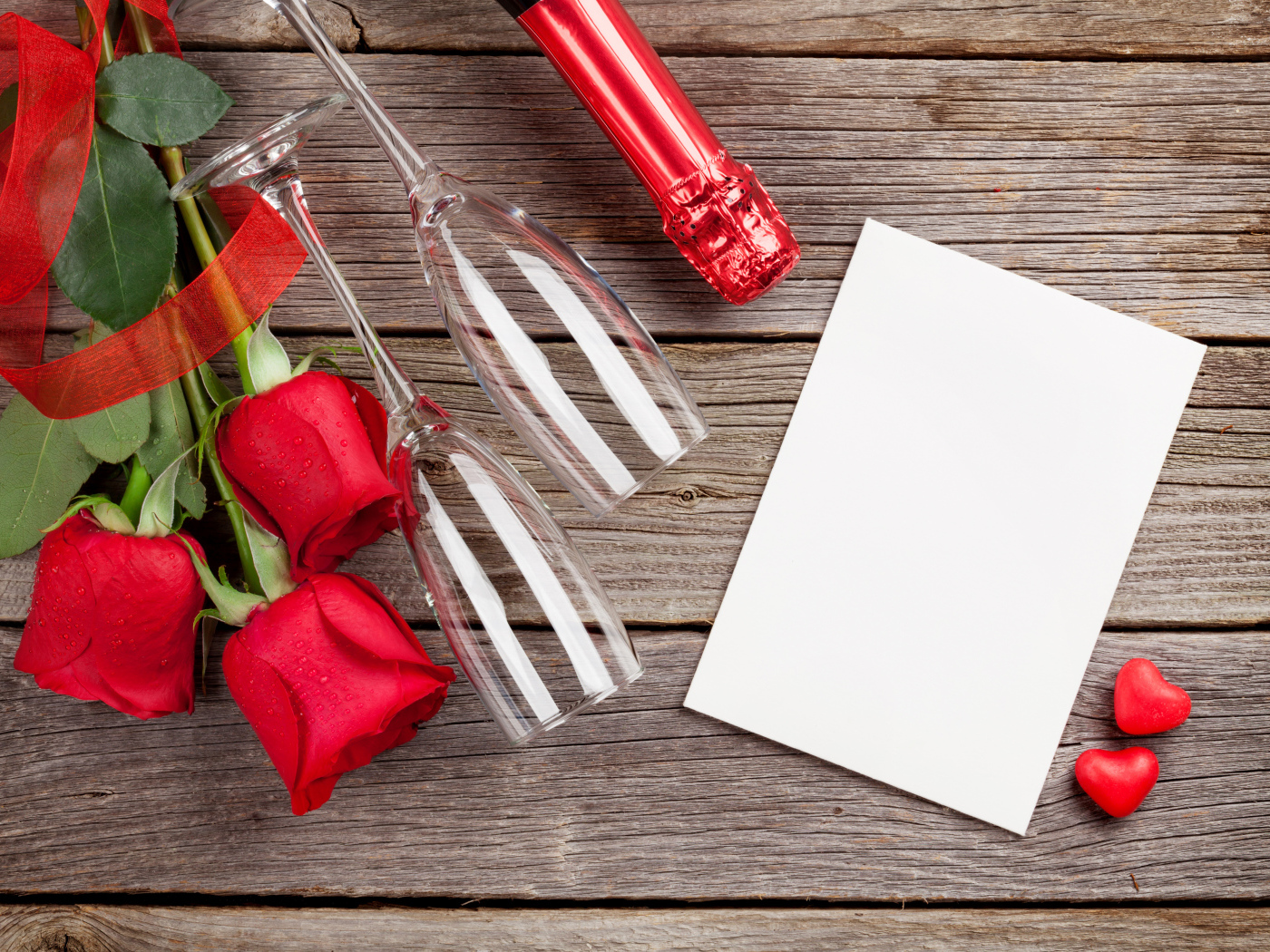 Белый лист бумаги на деревянном столе с бокалами и красными розами