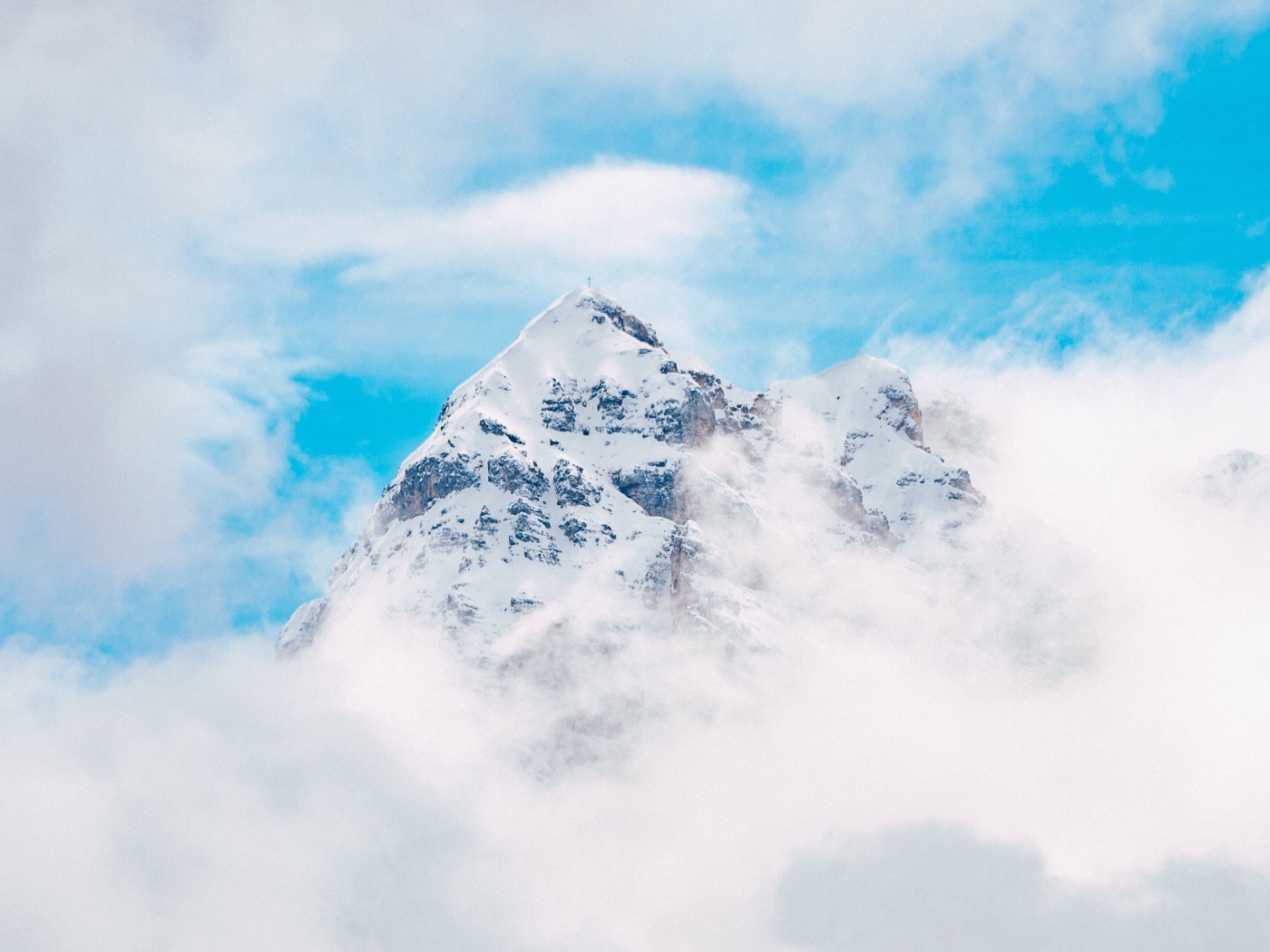 Заснеженная вершина горы в белых облаках под голубым небом