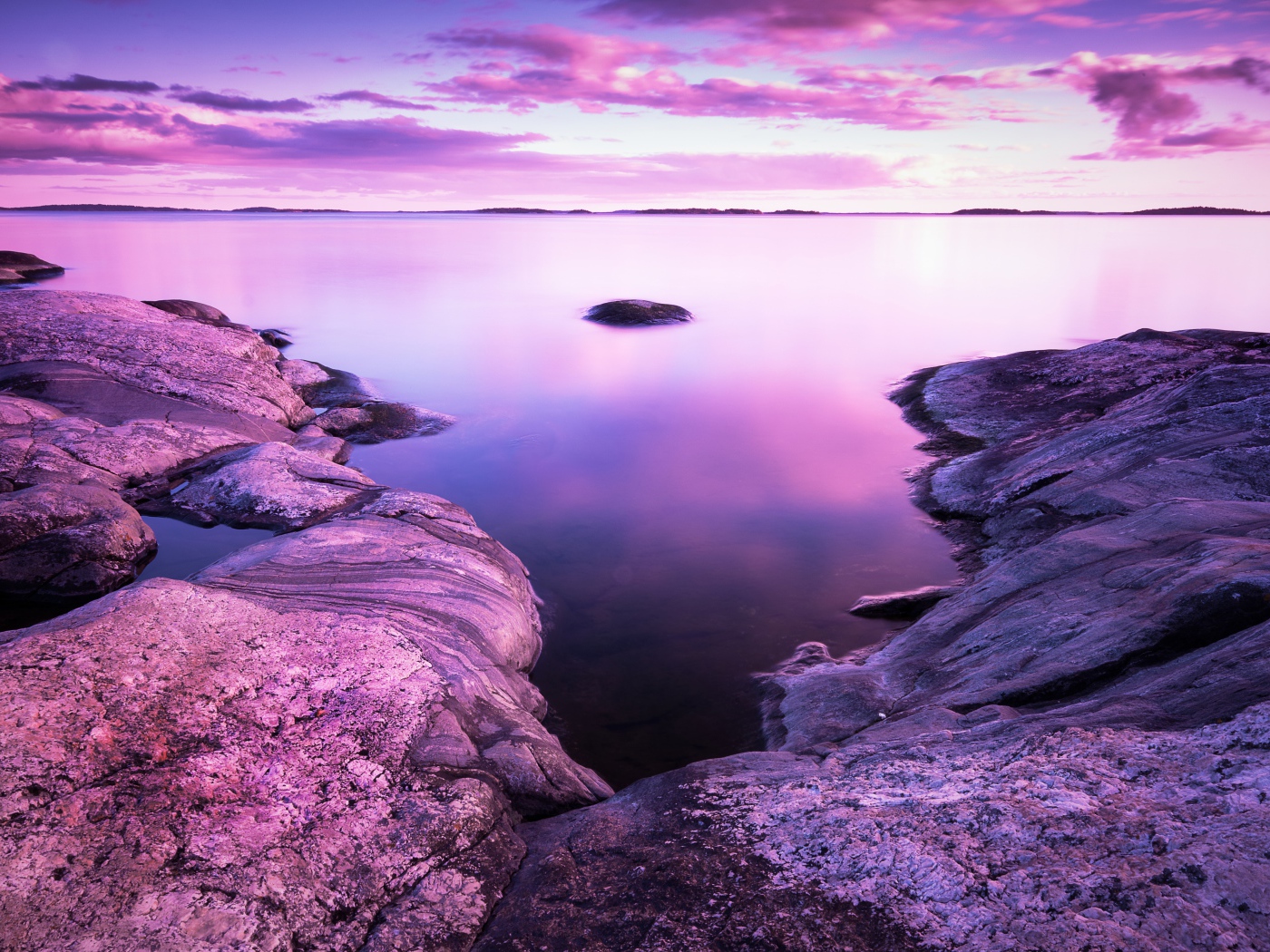 Сиреневый закат в небе над водой и камнями