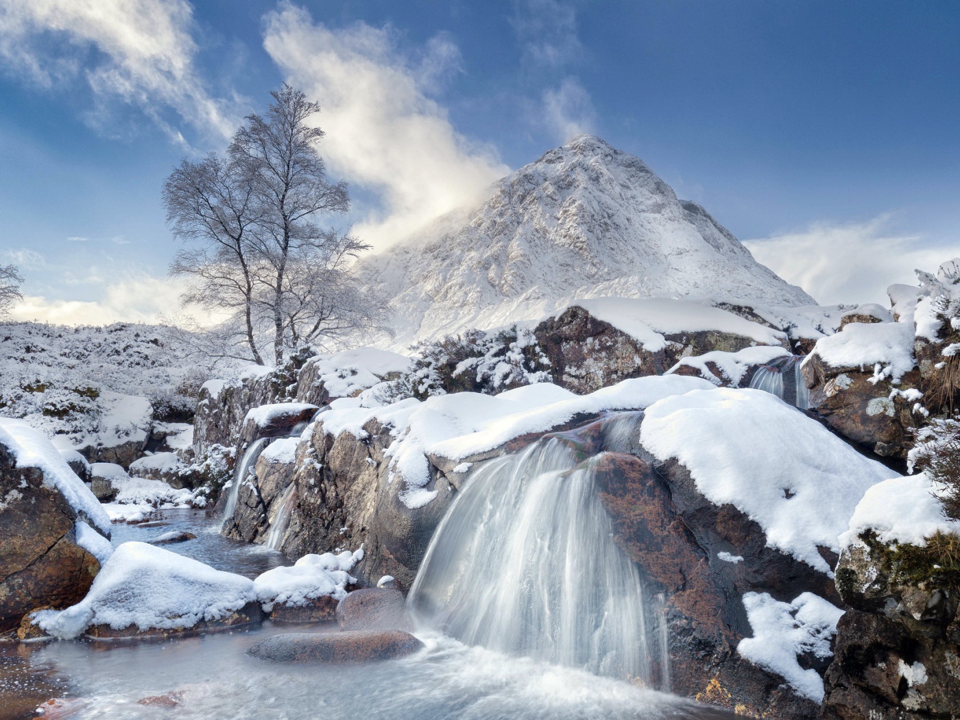 Водопад стекает с камней на фоне заснеженной горы