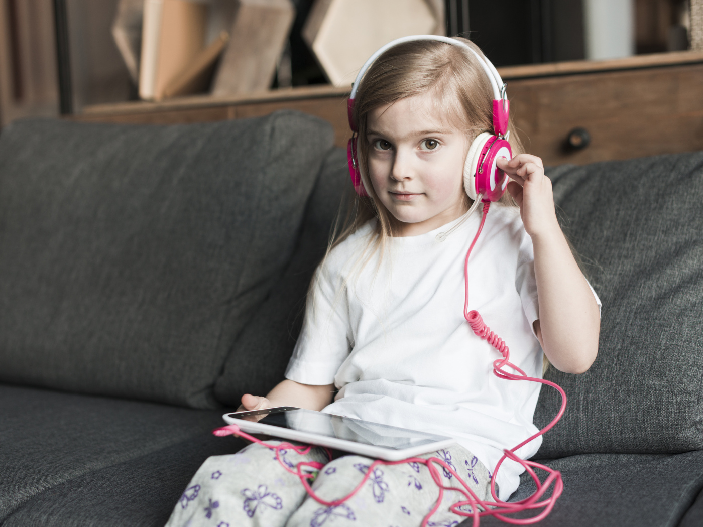 Девочка сидит на диване в наушниках  и с планшетом