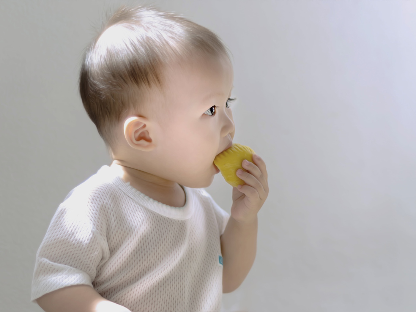 Маленький ребенок грызет игрушку на сером фоне