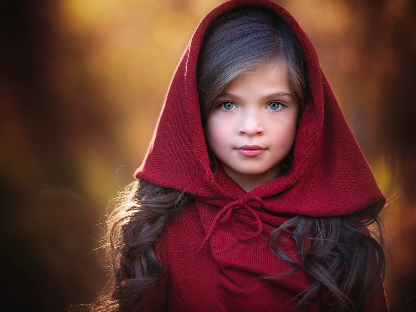 Маленькая красивая голубоглазая девочка с красным капюшоном на голове