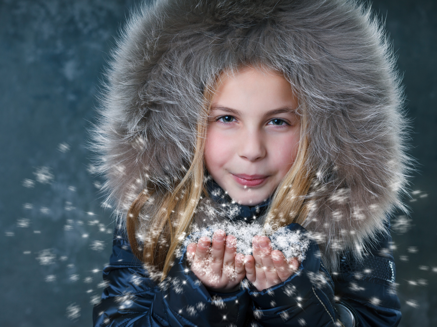 Маленькая девочка в капюшоне сдувает снежинки с ладоней