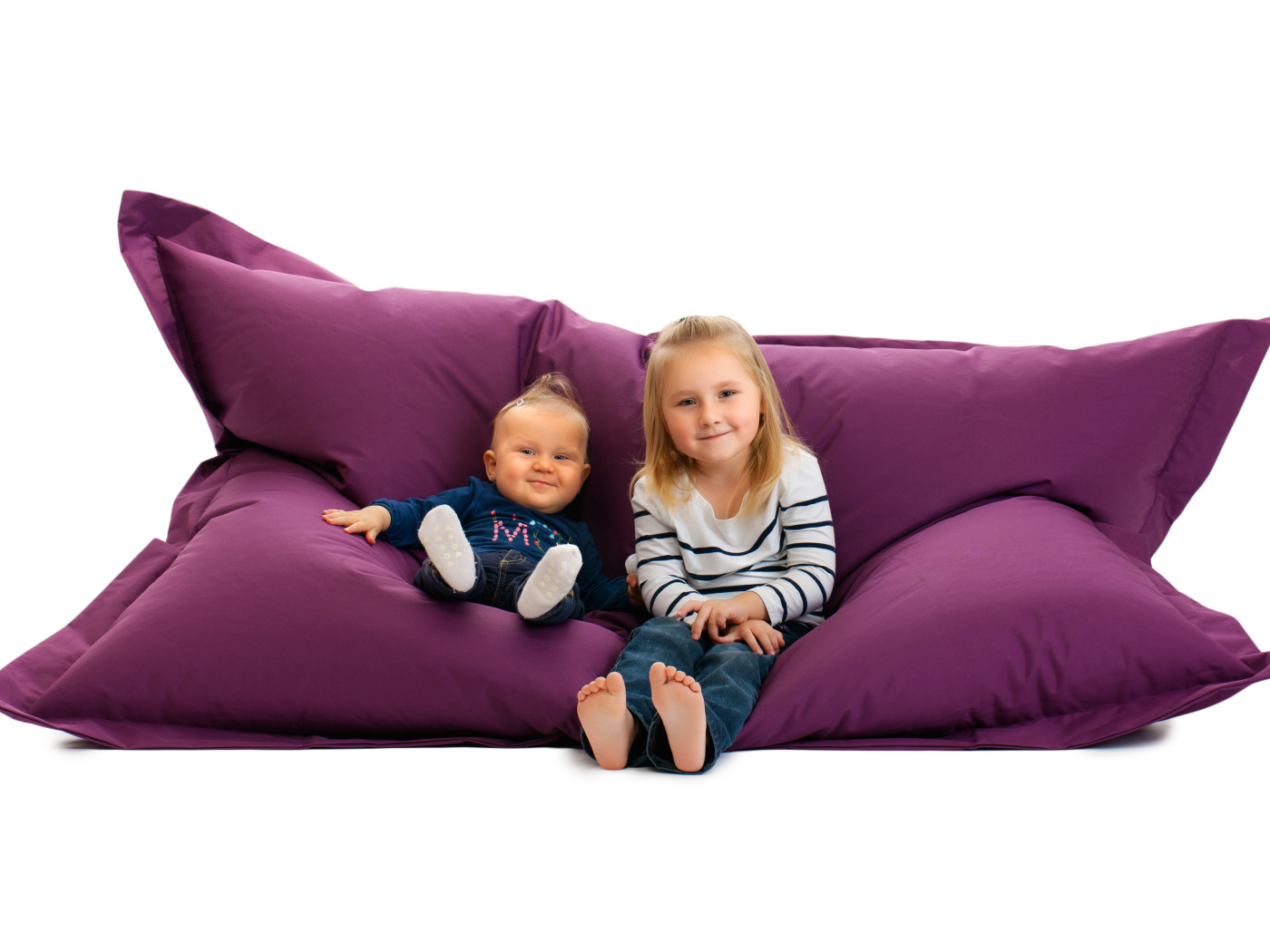 Маленькие девочки сидят на мягкой подушке на белом фоне