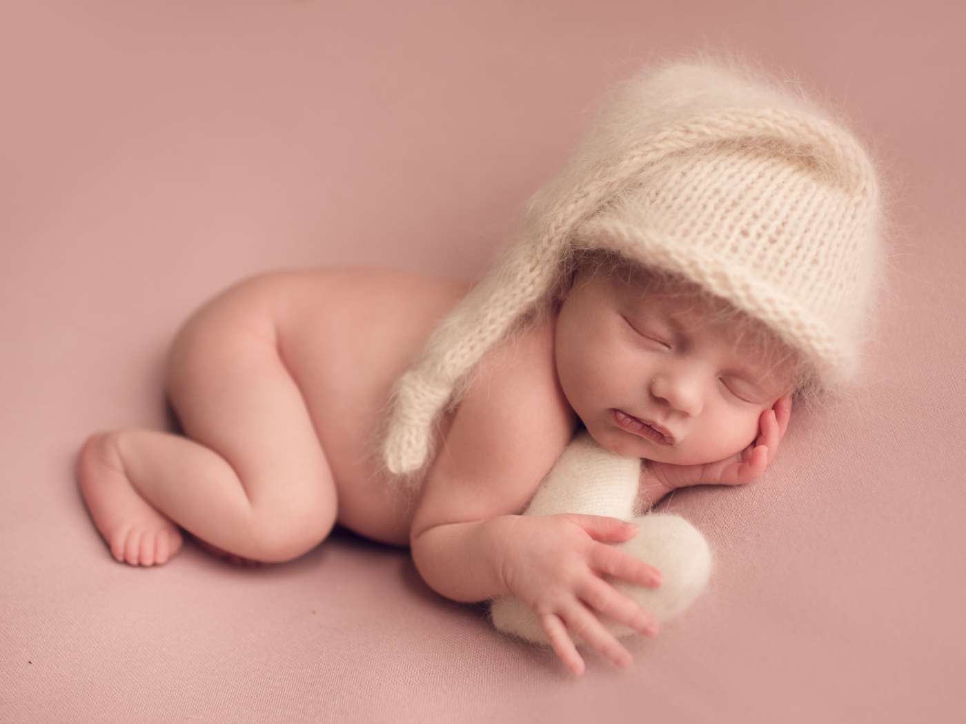 Маленький спящий ребенок в теплой шапке на розовом фоне
