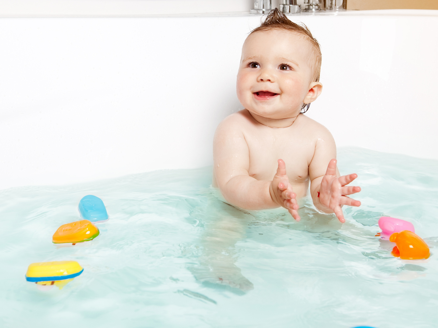 Маленький улыбающийся ребенок с игрушками в ванной 