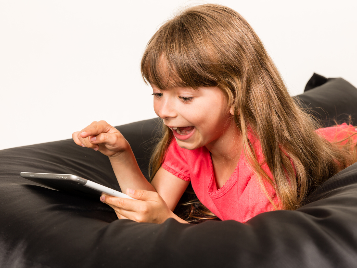Маленькая улыбающаяся девочка лежит с планшетом