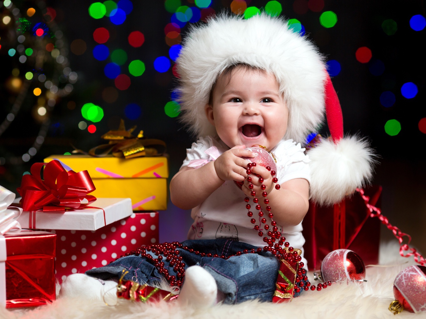 Улыбающийся малыш в новогодней шапке с подарками у елки