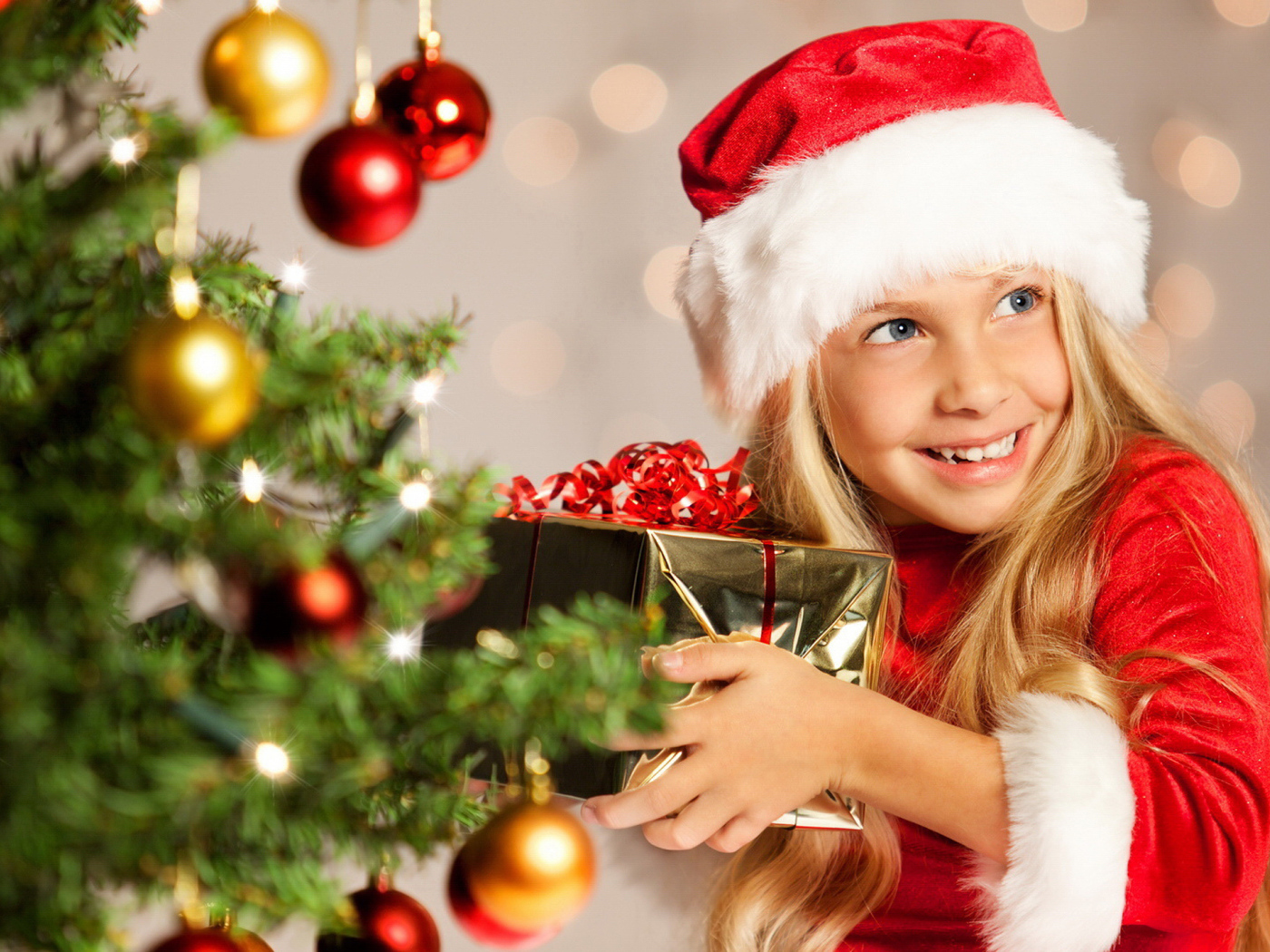 Улыбающаяся девочка блондинка с подарком у елки на новый год 