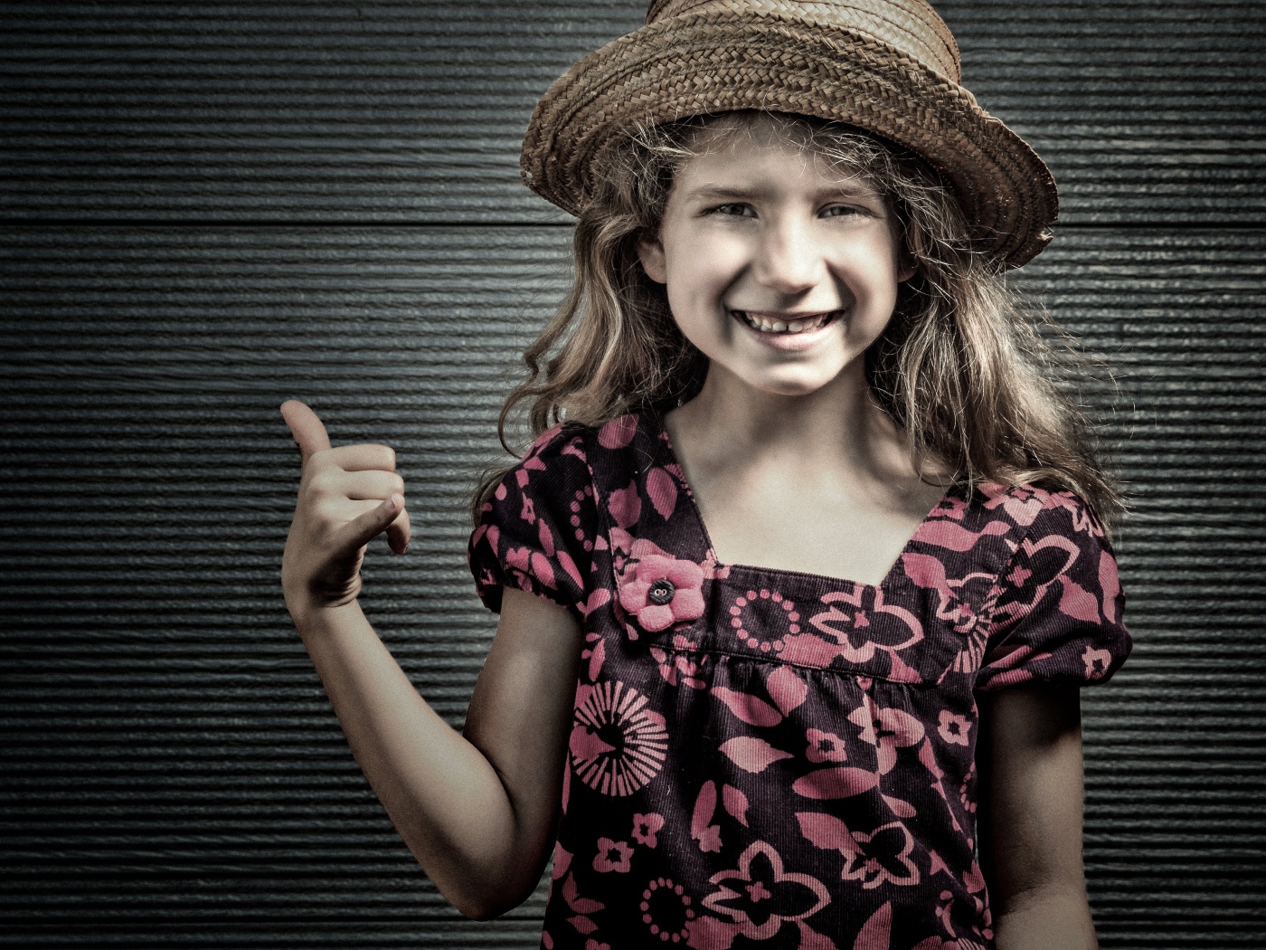 Улыбающаяся девочка в соломенной шляпе у стены 