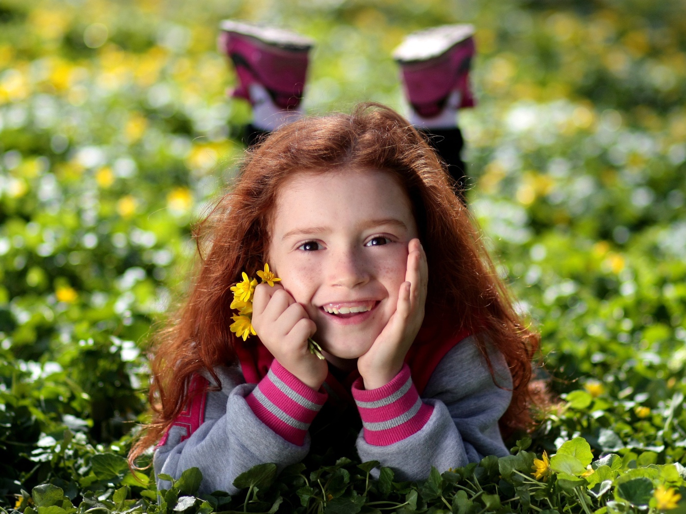 Улыбающаяся рыжеволосая девочка лежит на зеленой траве